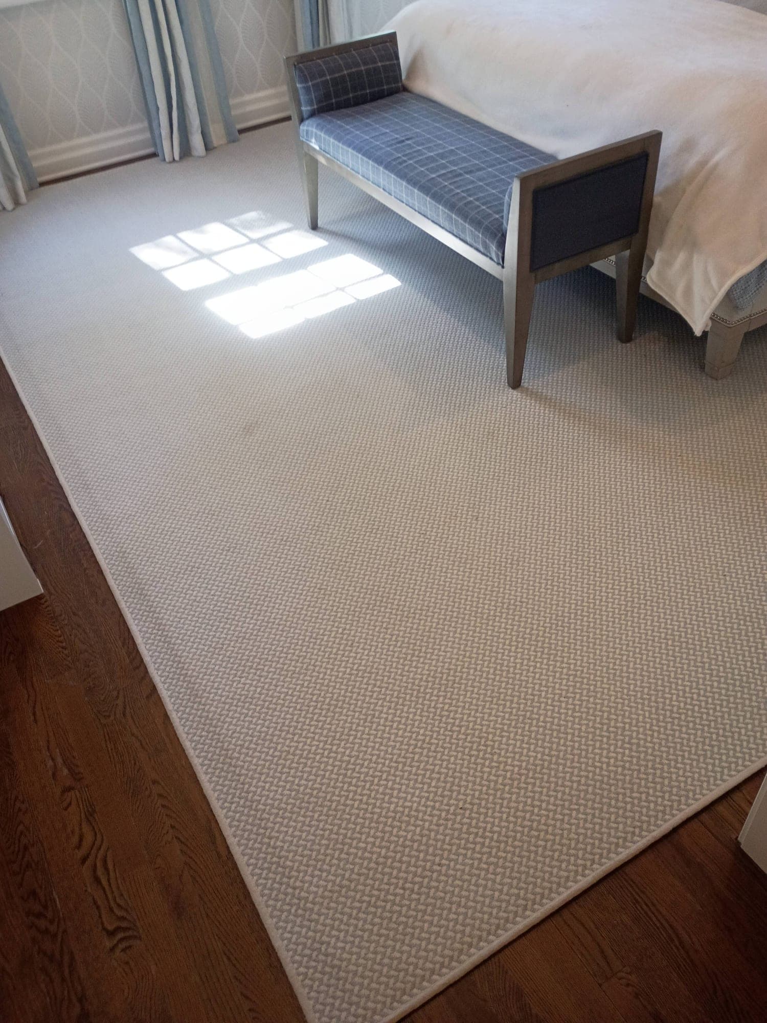 Light-filled bedroom with area rug, bench and bed before cleaning