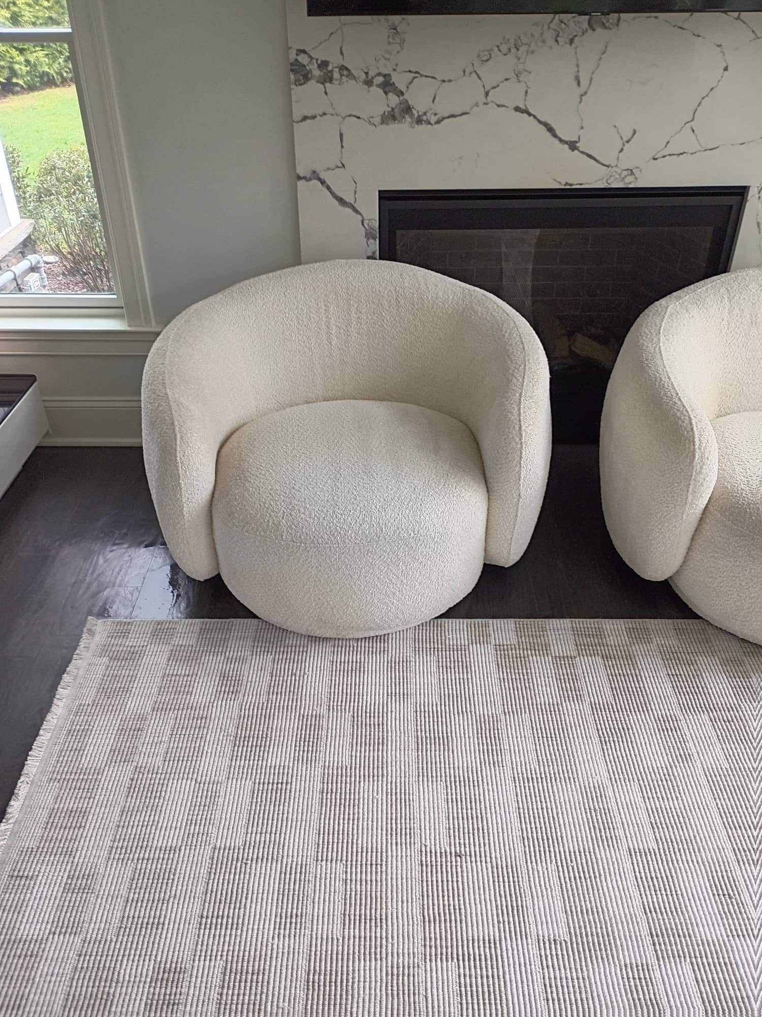Matching white boucle swivel chairs beside fireplace and window