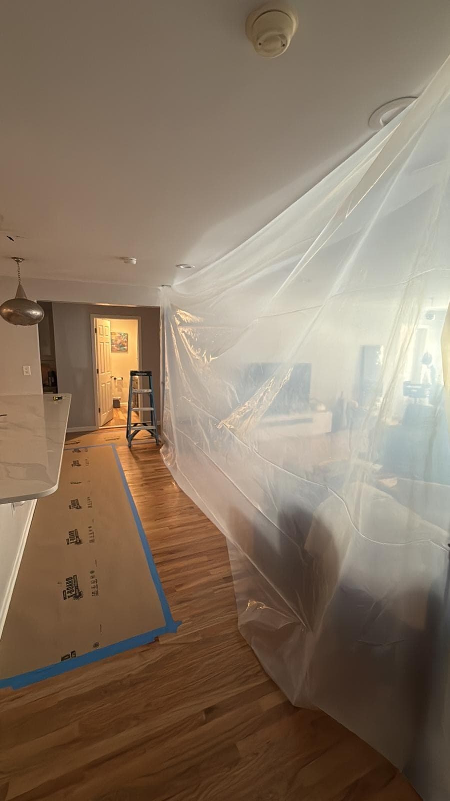 Floor-to-ceiling poly containment barrier with taped floor protection in a kitchen hallway