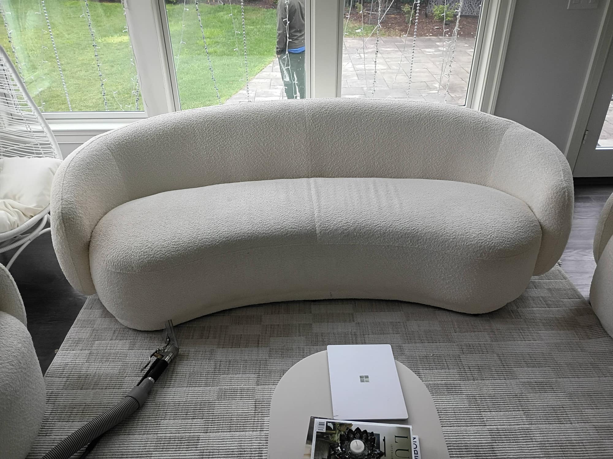 Curved white boucle sofa facing a backyard patio with string lights