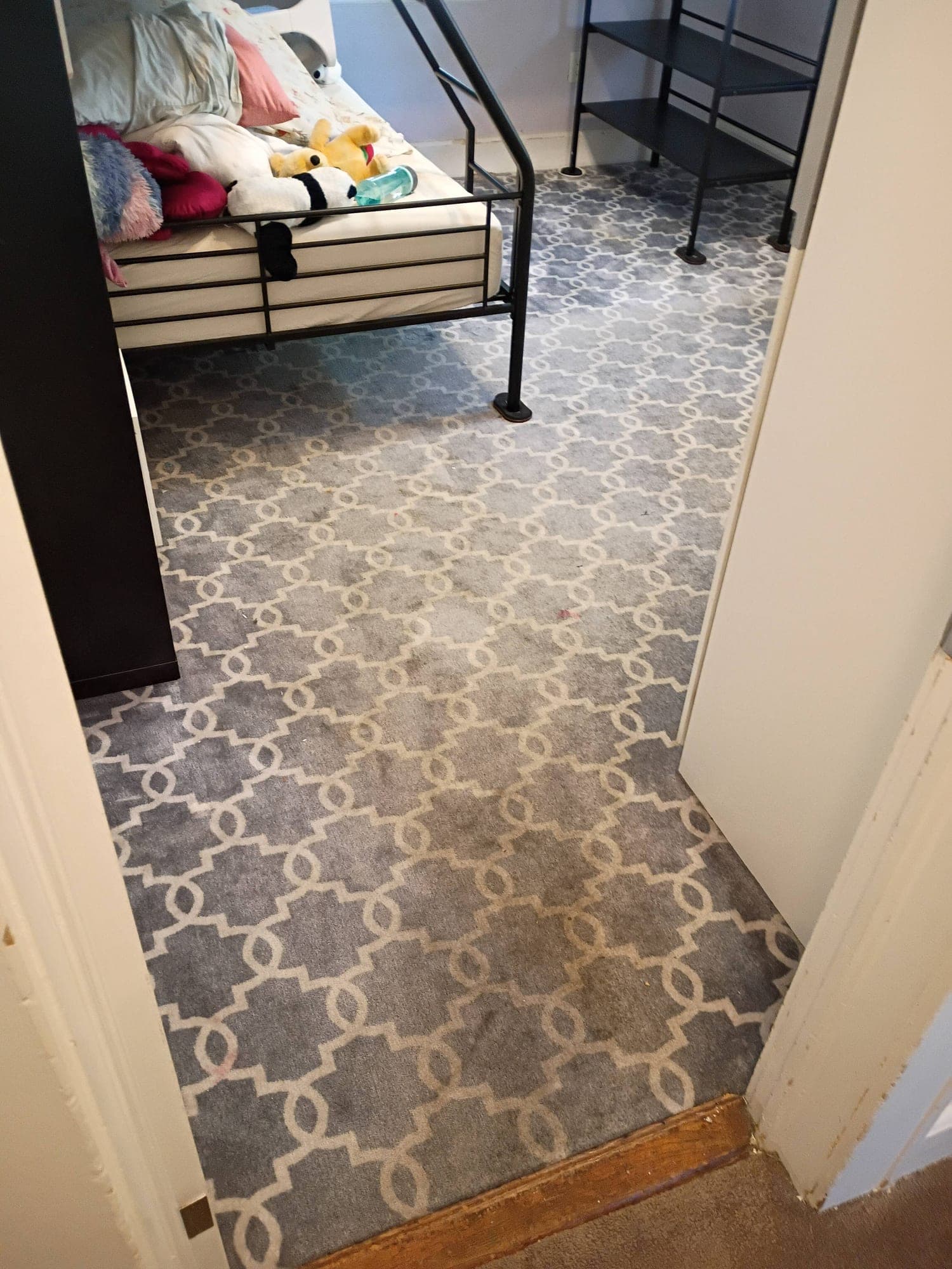 Kid's bedroom with patterned carpet, bed and stuffed animals before cleaning