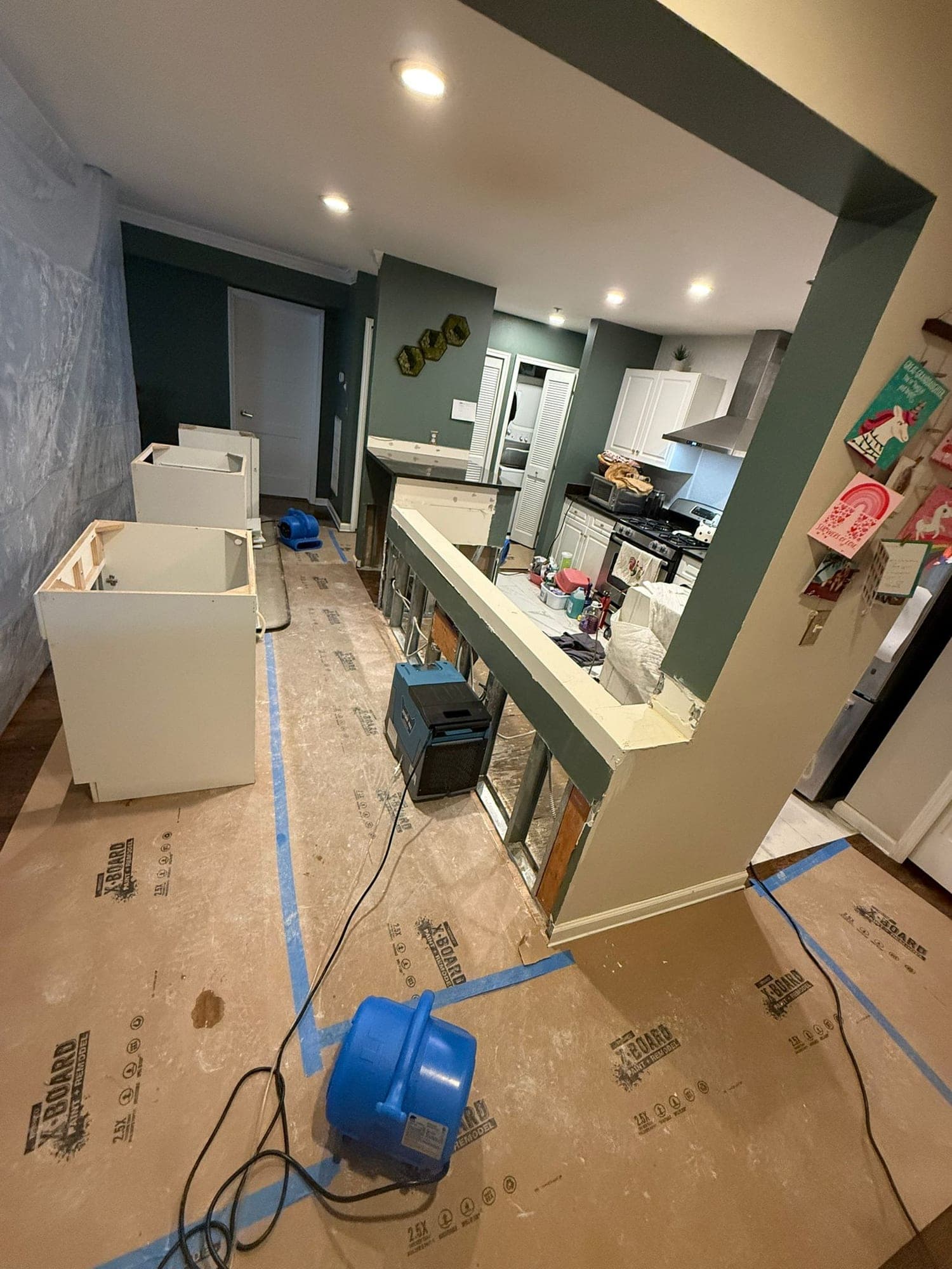 Kitchen half-wall opened to studs with air mover, dehumidifier and floor protection during drying