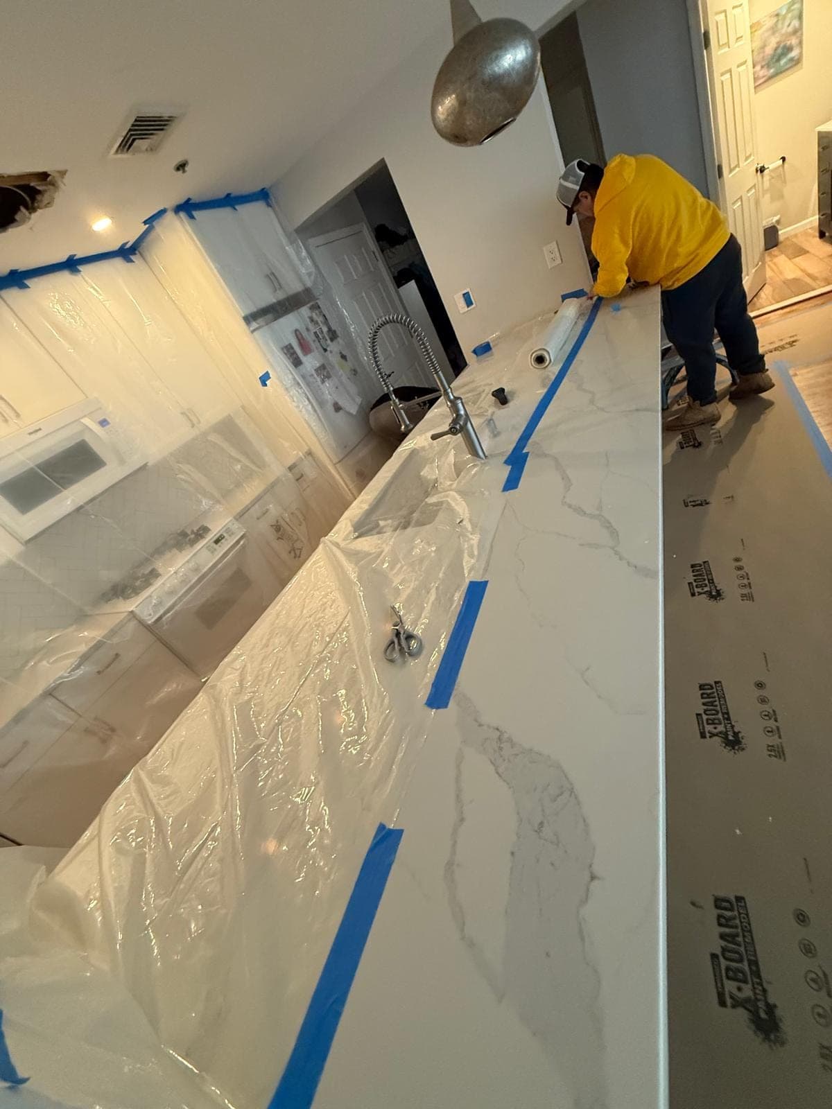 Technician taping protective sheeting and board over a kitchen island before water damage demolition