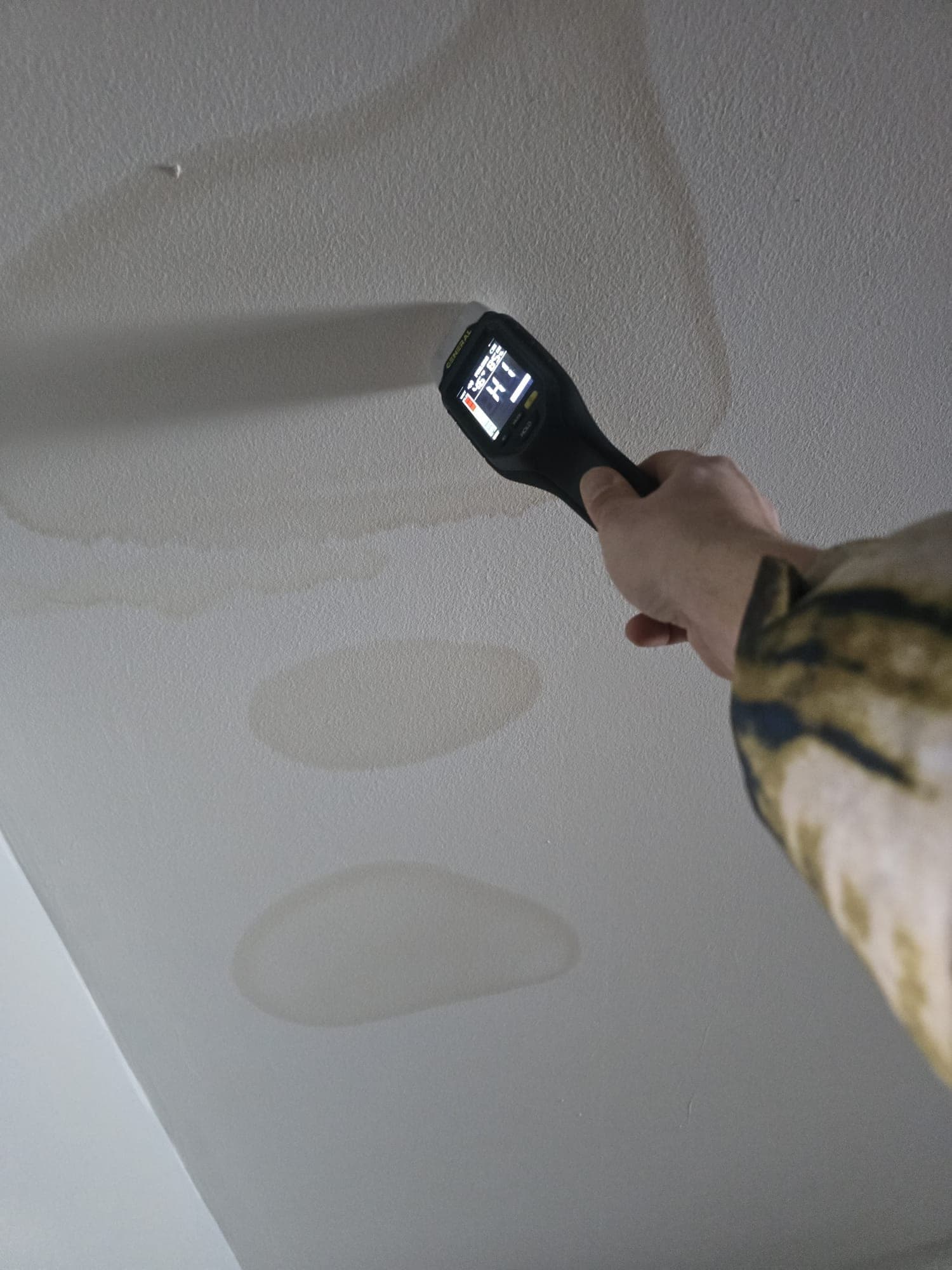Moisture meter reading high against a ceiling marked with water stain rings