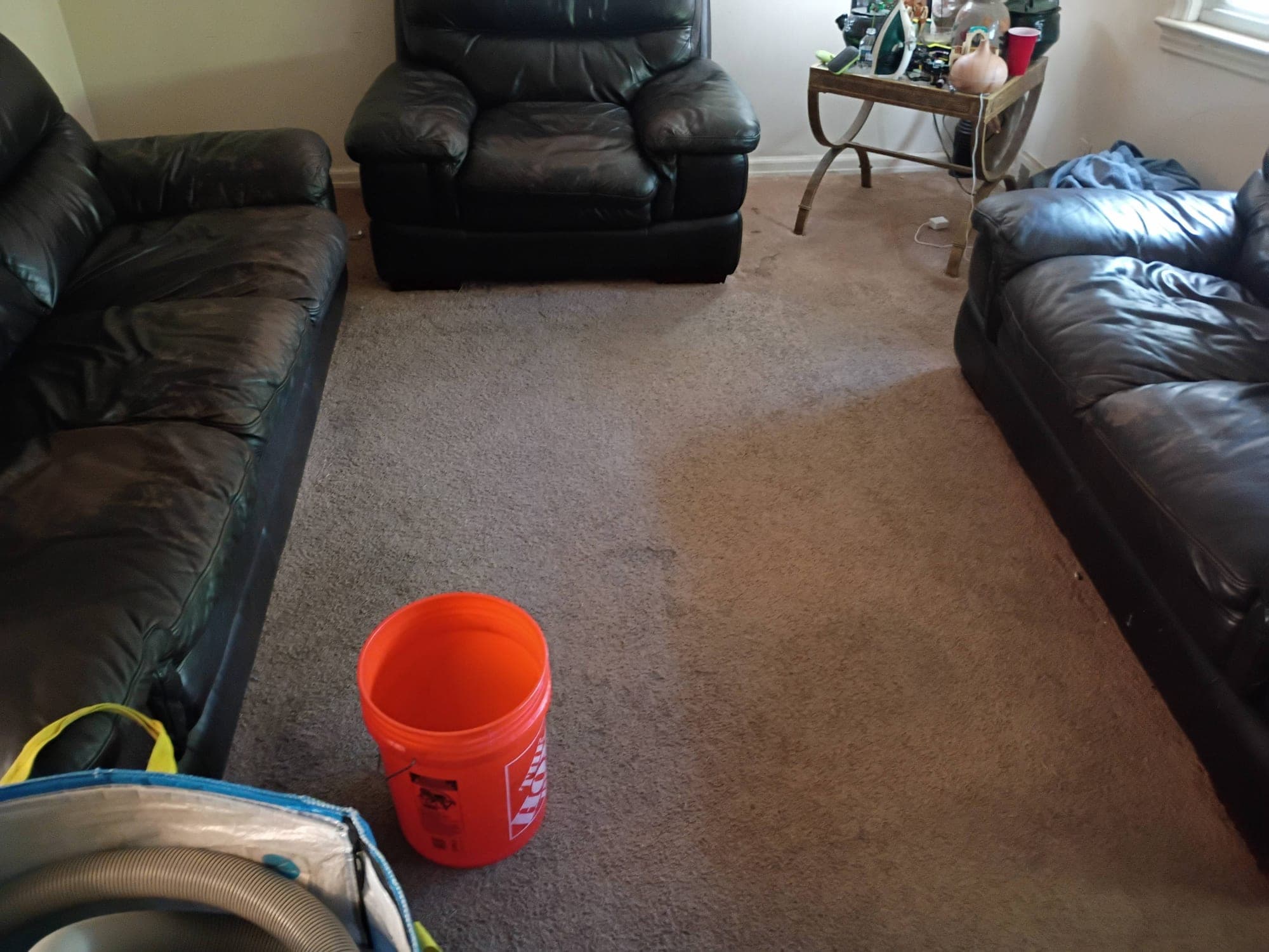 Living room with black leather couches and stained carpet before cleaning