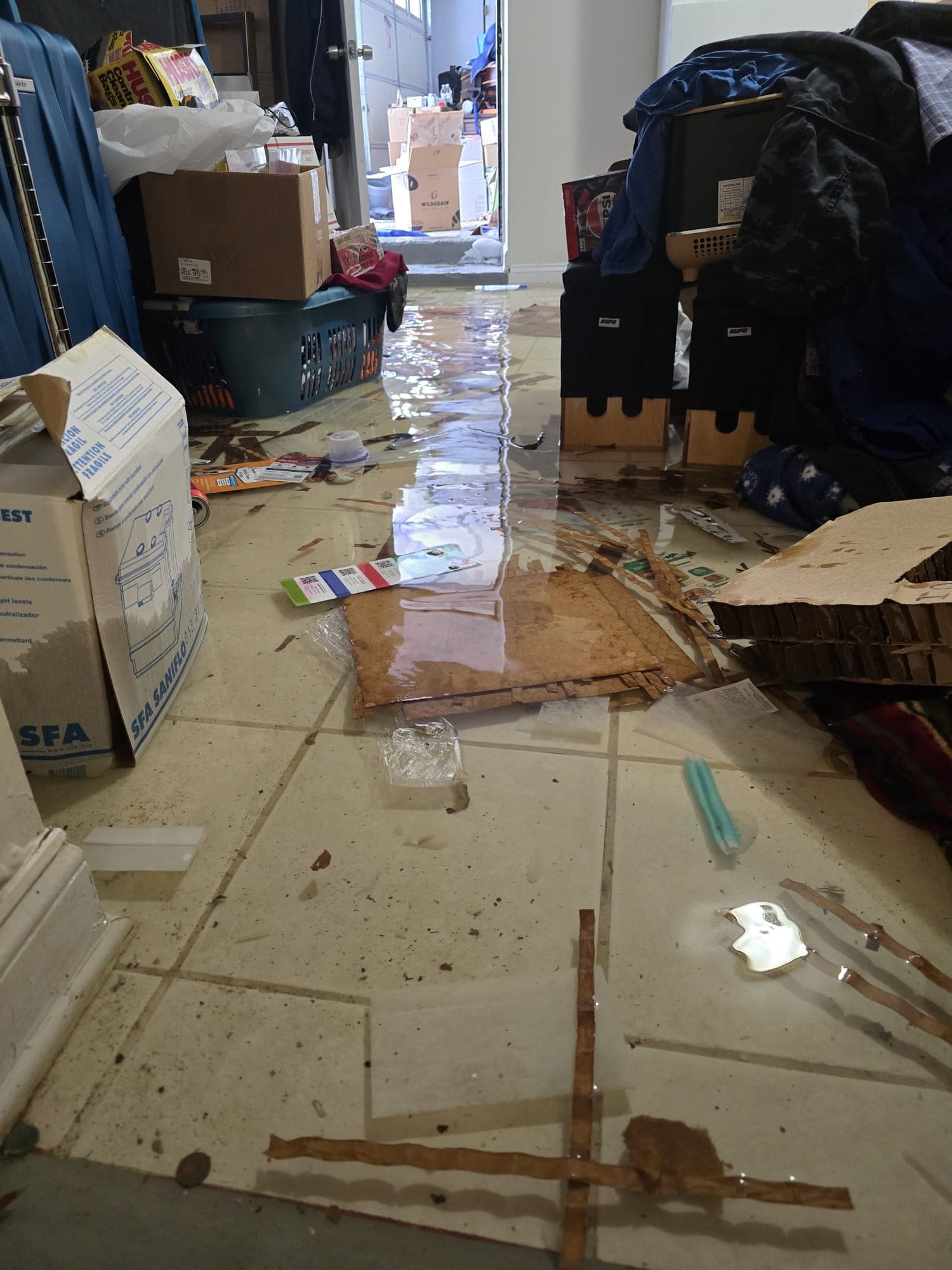 Sheet of standing water across a basement floor with soaked cardboard and belongings