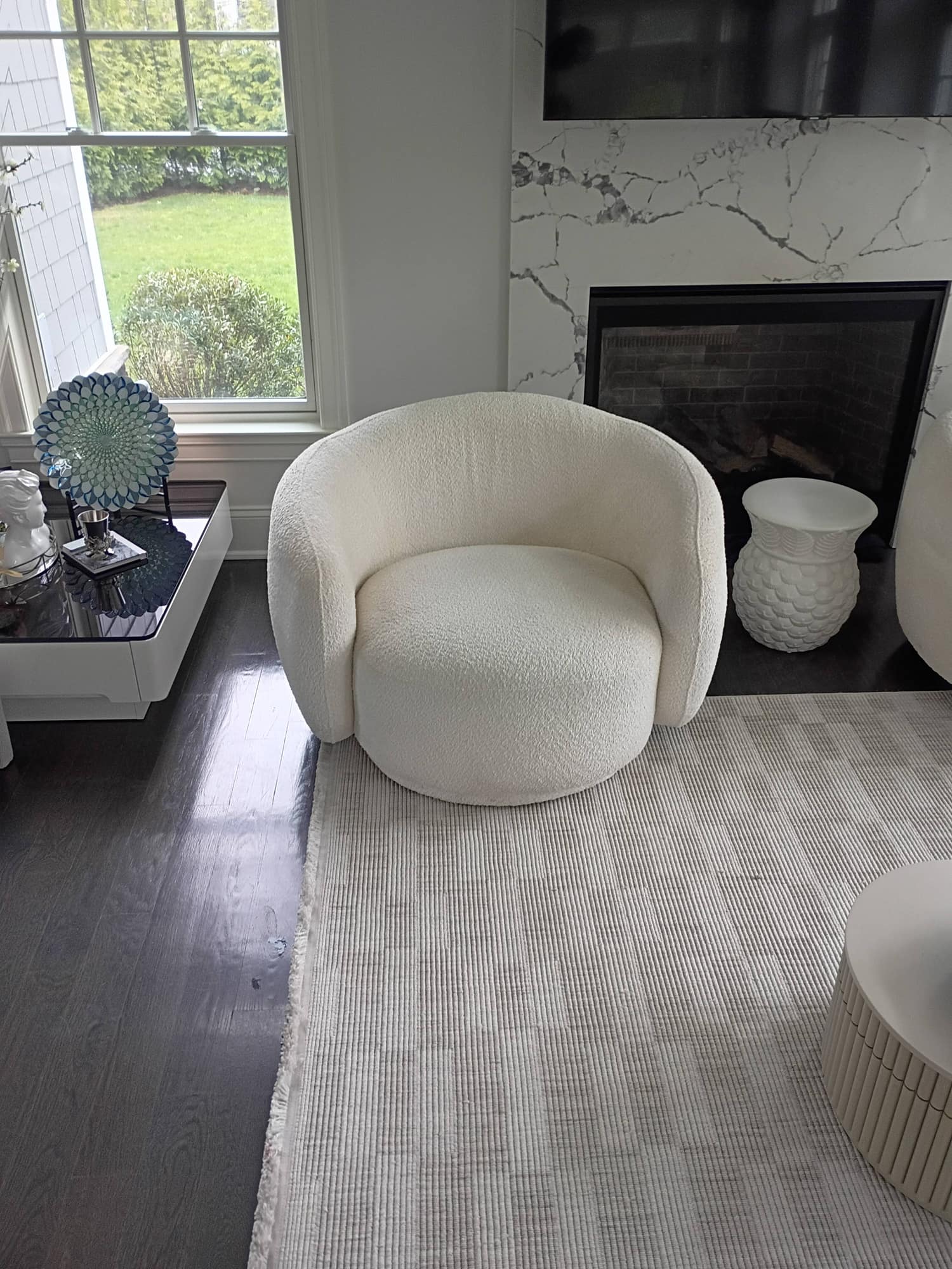 Two white boucle swivel chairs facing a marble fireplace and window