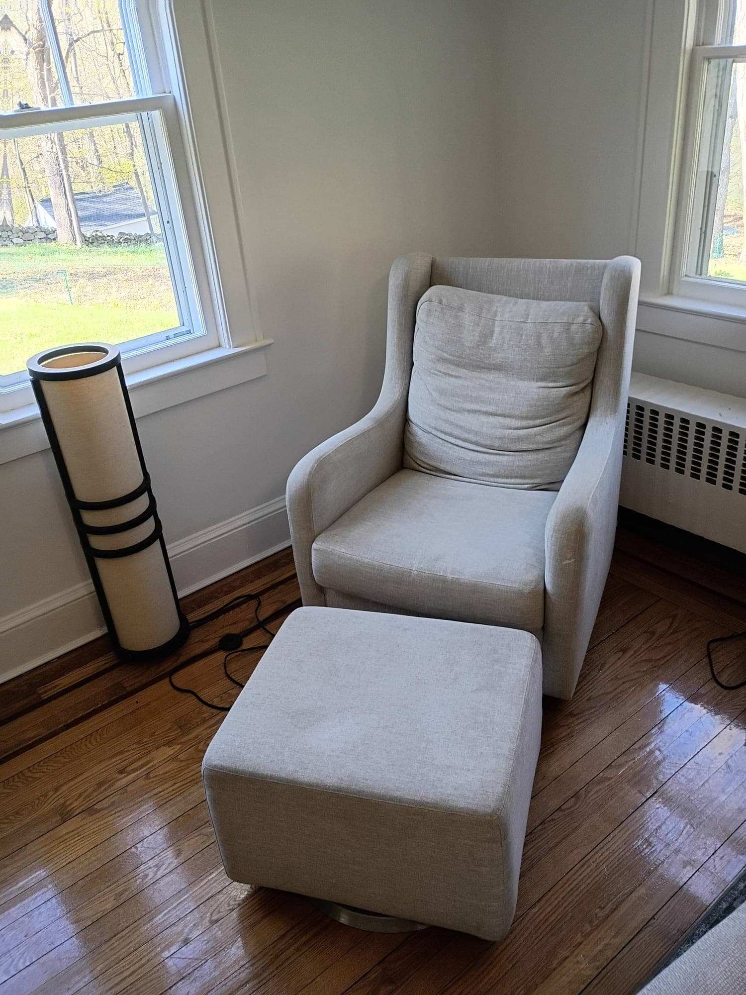 Gray wingback armchair with ottoman in a sunlit corner before cleaning
