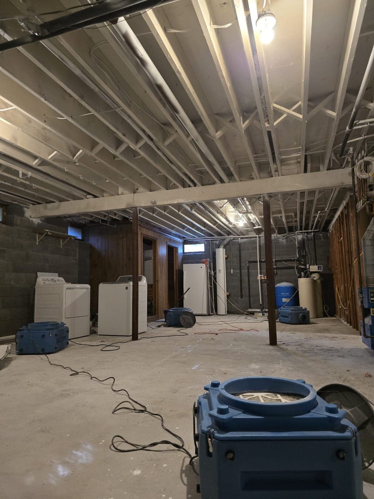 Air movers drying a gutted basement with exposed joists and block walls