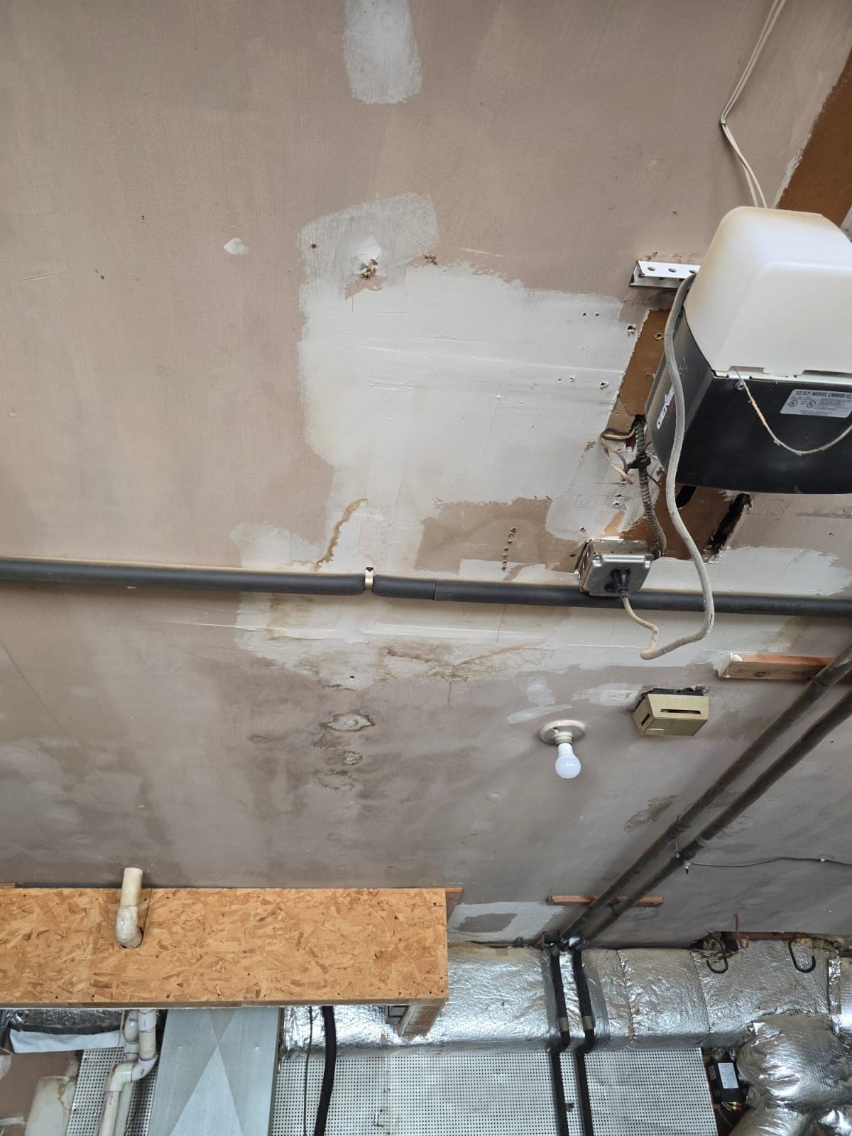 Water stains spreading across a garage ceiling beneath supply pipes and a garage door opener after a pipe leak