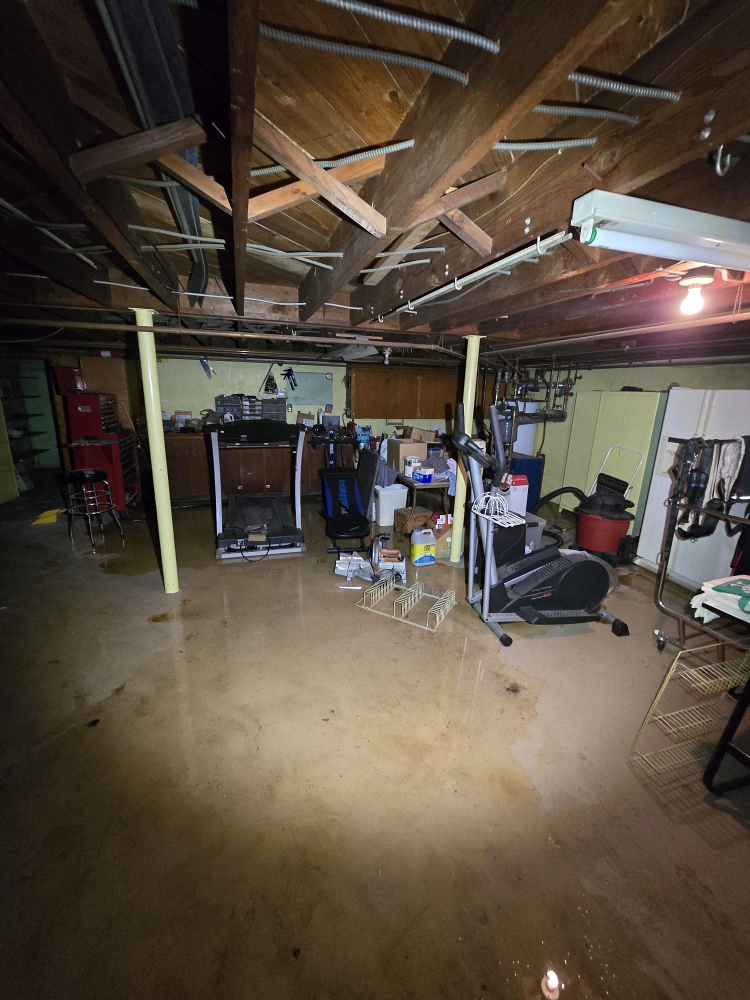 Flooded basement with water sheeting across the floor around exercise equipment and stored belongings