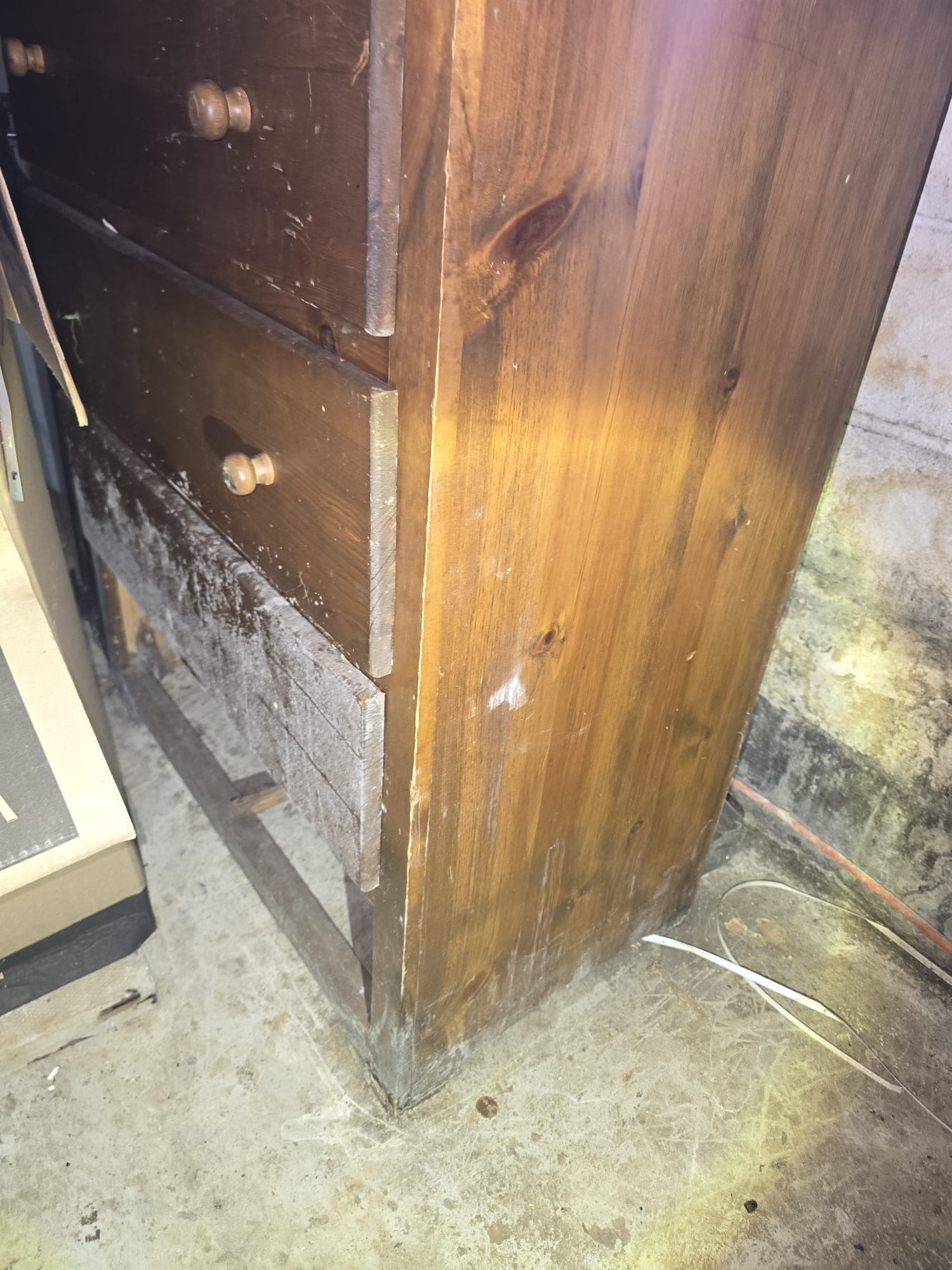 Mold growing across the side of a wooden dresser in a damp basement