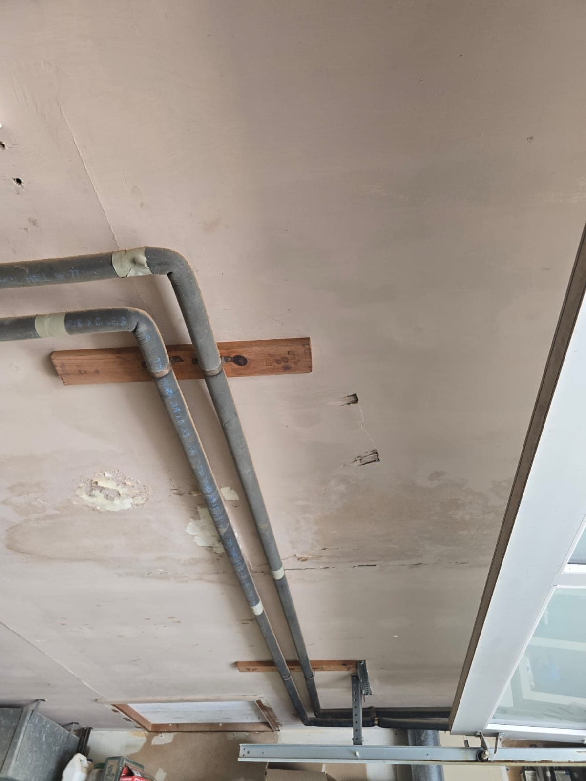 Copper and black supply pipes crossing a ceiling stained by a pipe leak