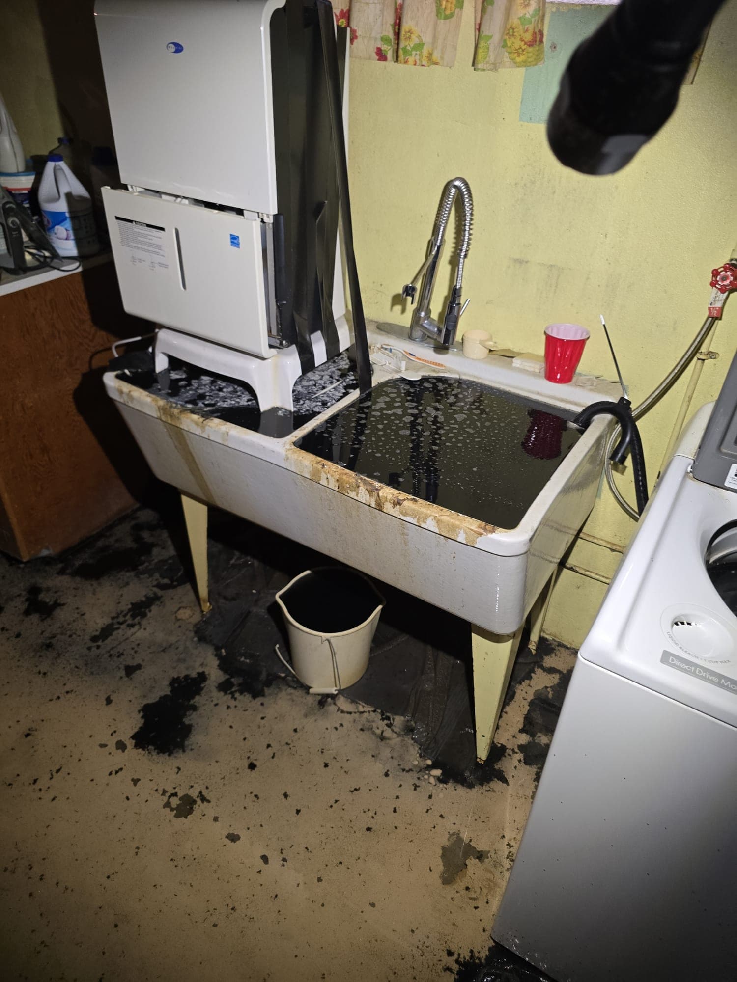 Sewage backup filling a basement laundry sink with black wastewater and spilling onto the floor