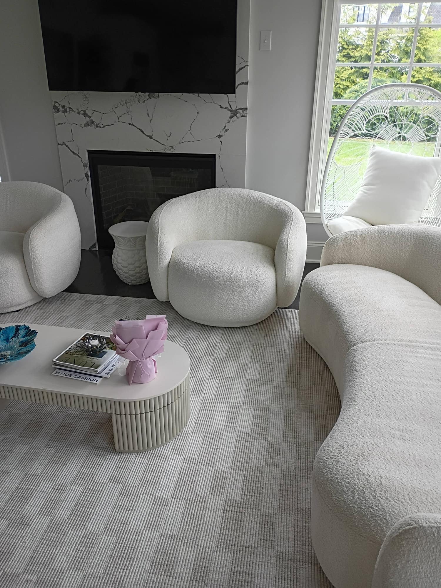 Bright sunroom with white boucle chairs, sofa and hanging egg chair before carpet cleaning