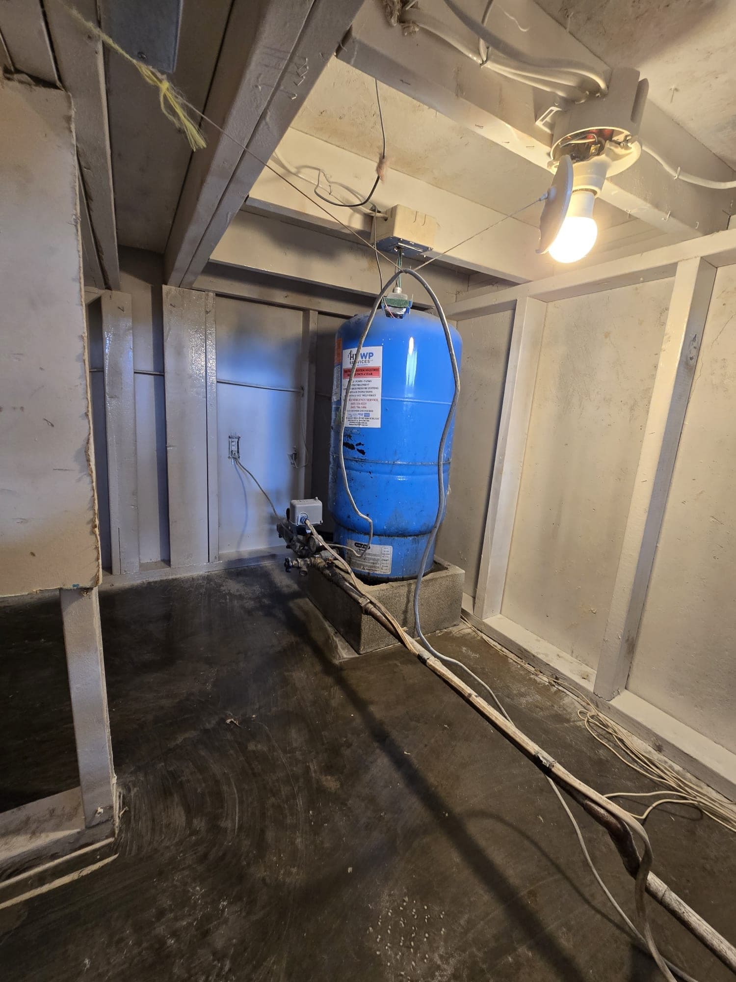 Well pressure tank and supply lines in a utility room with water pooled on the floor