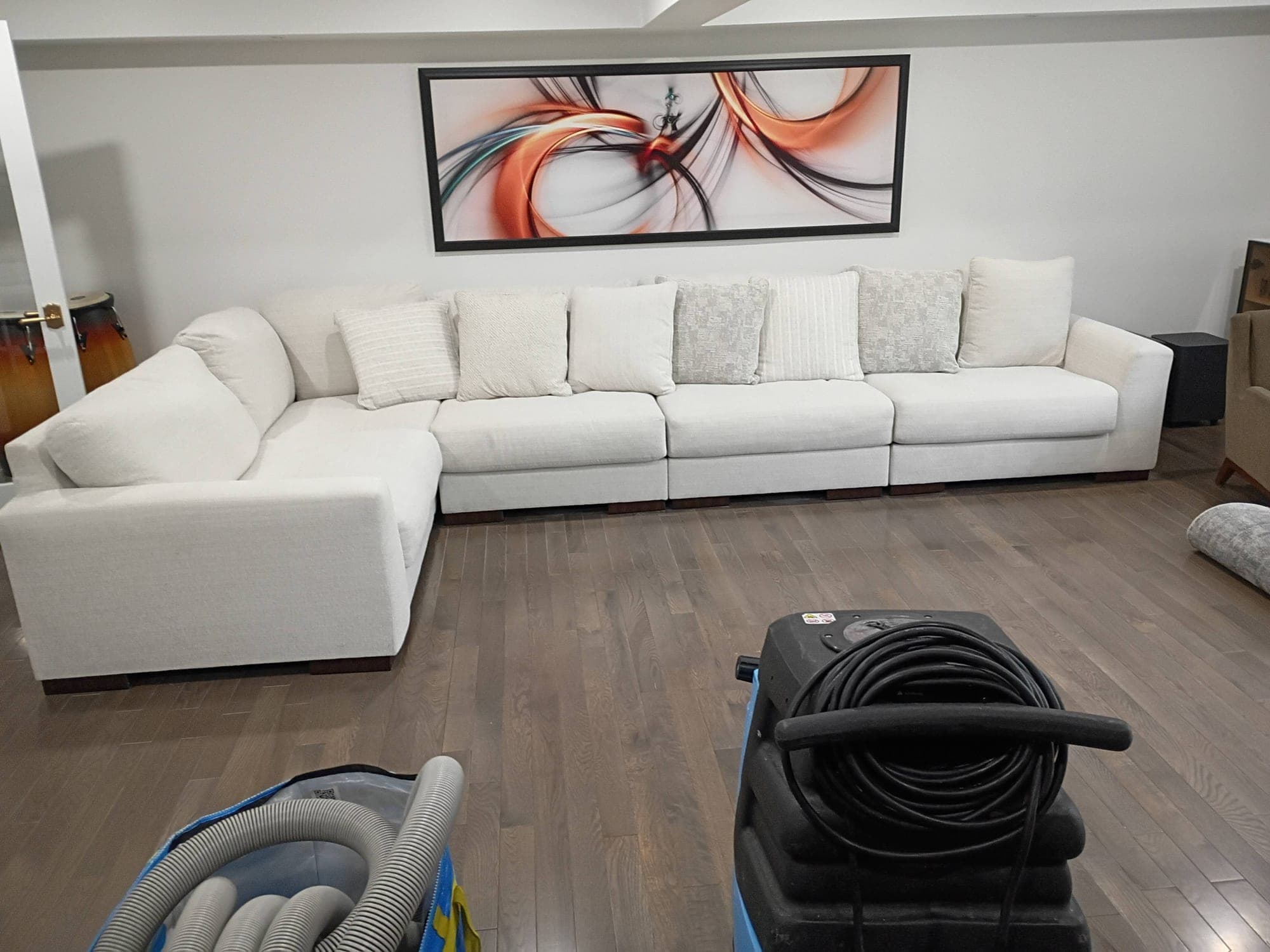 Living room with white sectional sofa and carpet cleaning equipment hoses